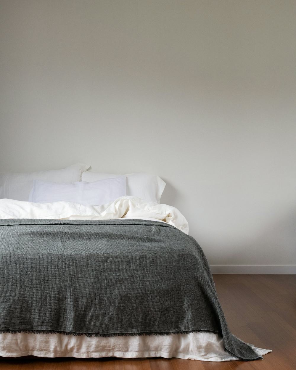 Quarto claro com cama arrumada e manta cinza sobre o colchão