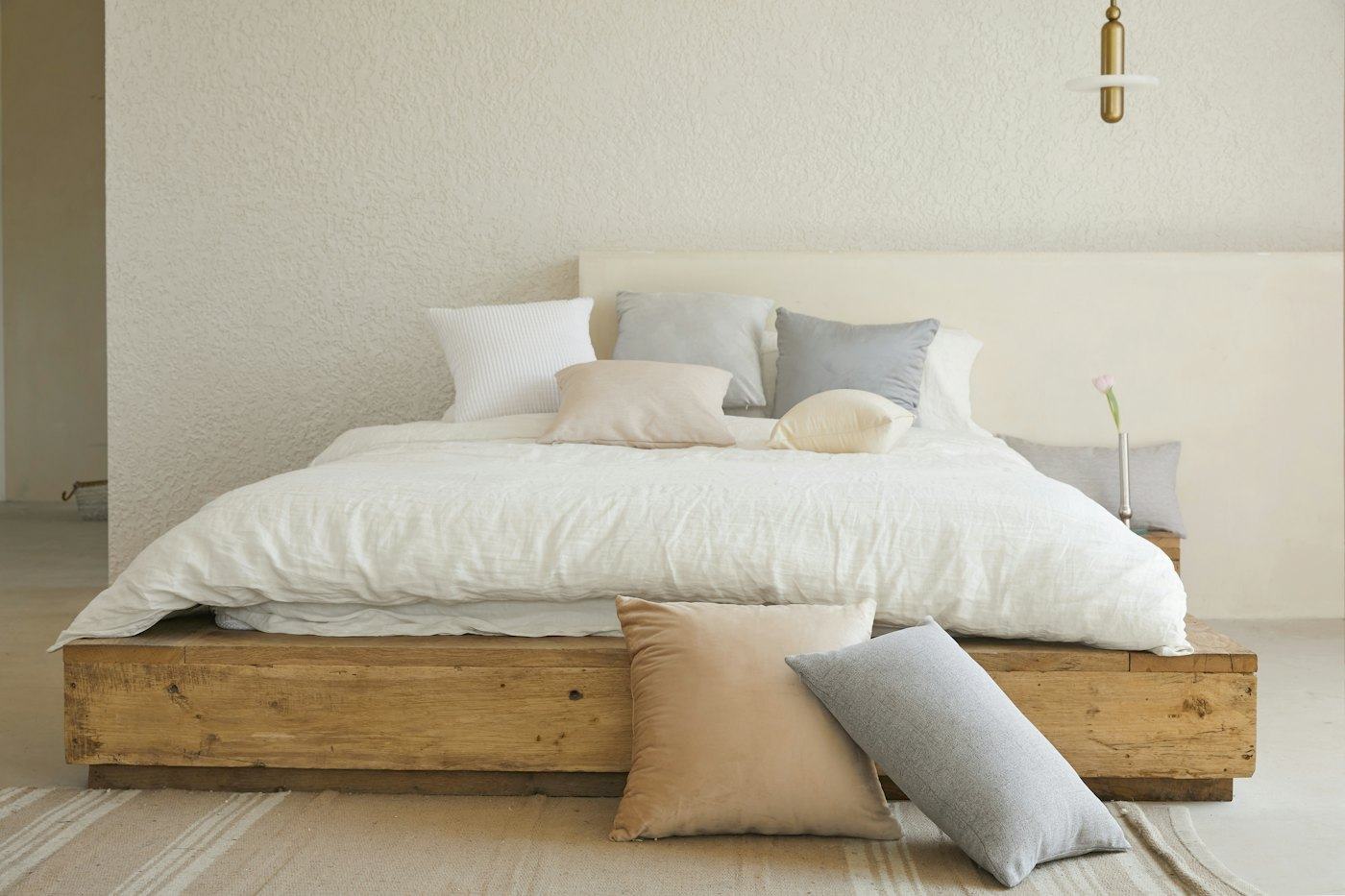 Cama de madeira com roupa de cama branca e almofadas em tons de areia e cinza